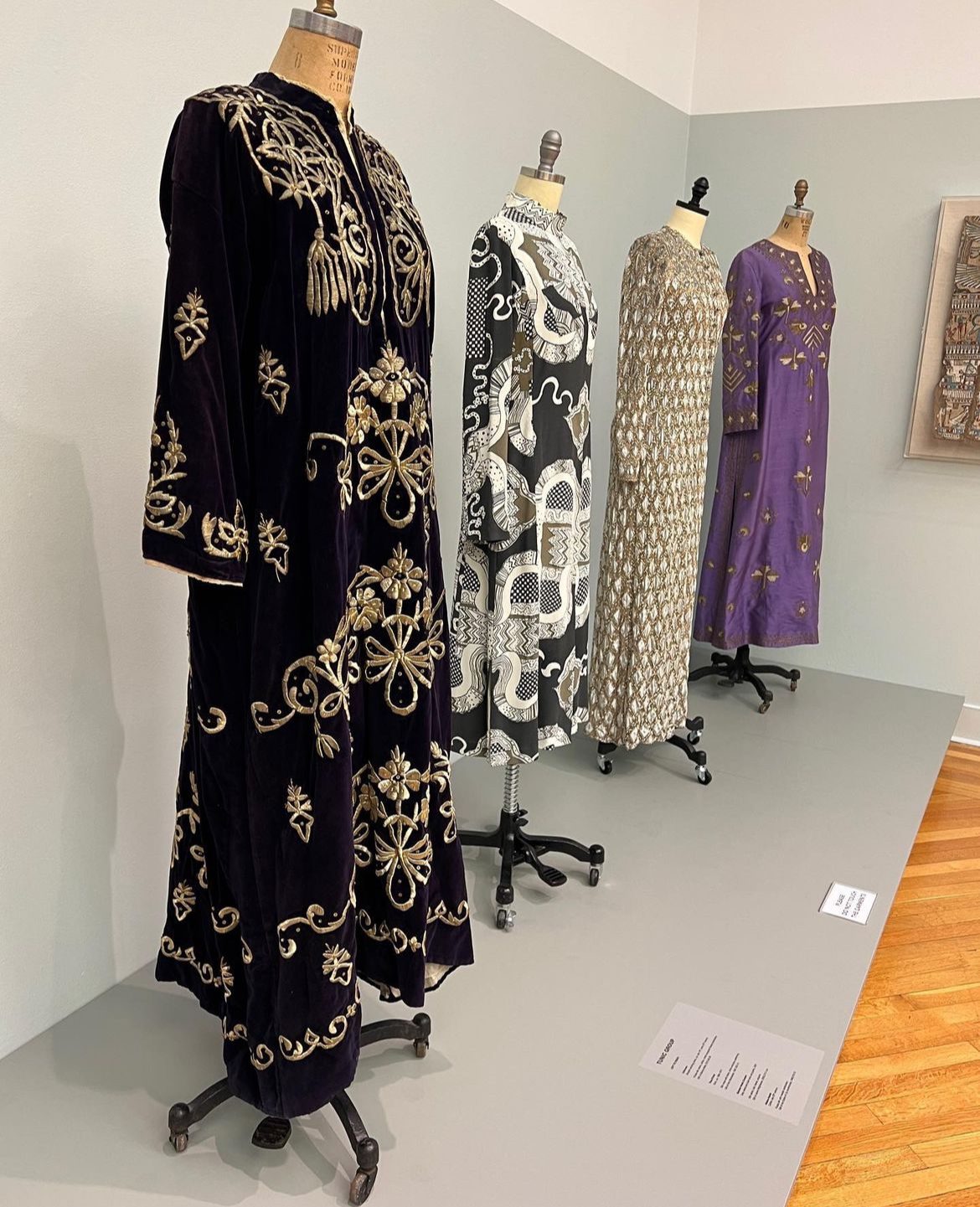 6 IMG_9079EB90076C-1 Thawbs at an exhibit. From left to right; Dark purple velvet with gold beading and embellishments, a black and white abstract pattern, a gold and grey with beading, and Purple silk with gold beadings.