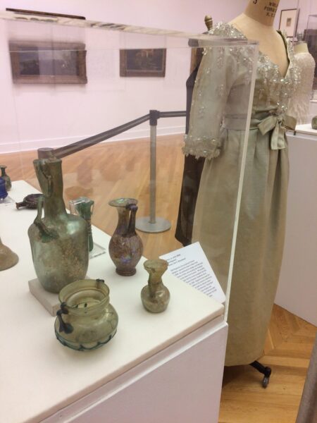 A grey silk dress with a beaded bodice next to some artifacts at a museum.