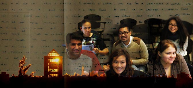 A stylistic photo of people sitting in a classroom on the right-hand side and the Queens College Library on the left-hand side.  The backdrop contains written text.