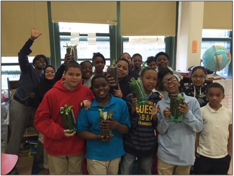 A group photo of students holding a garden, which was planted in recycled soda bottles.