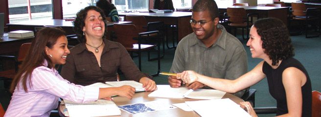 Four people sitting at a table studying with their notebooks open.