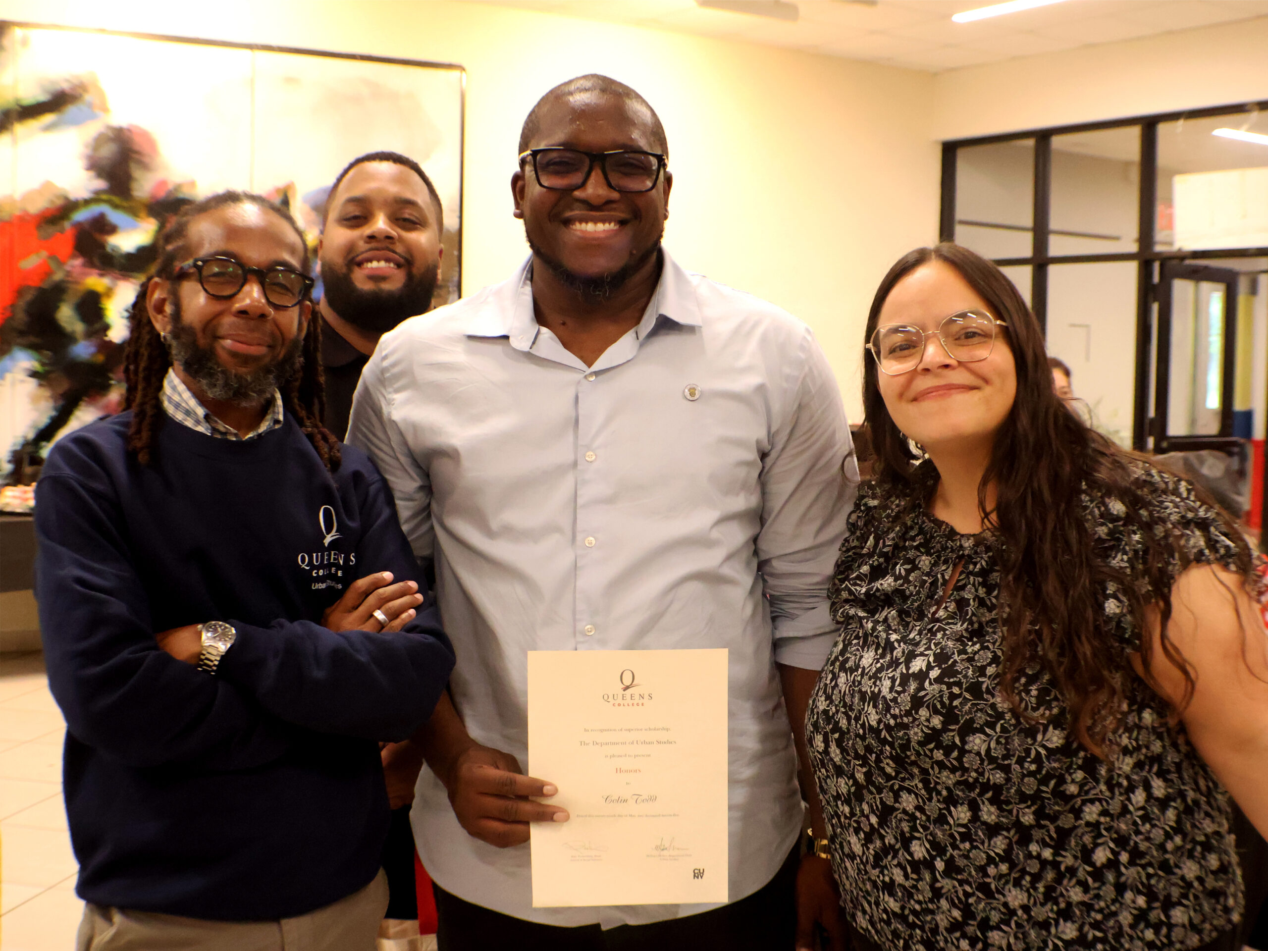 Four people, the person in the center is holding a certificate during 2025 Graduation Award Ceremony.