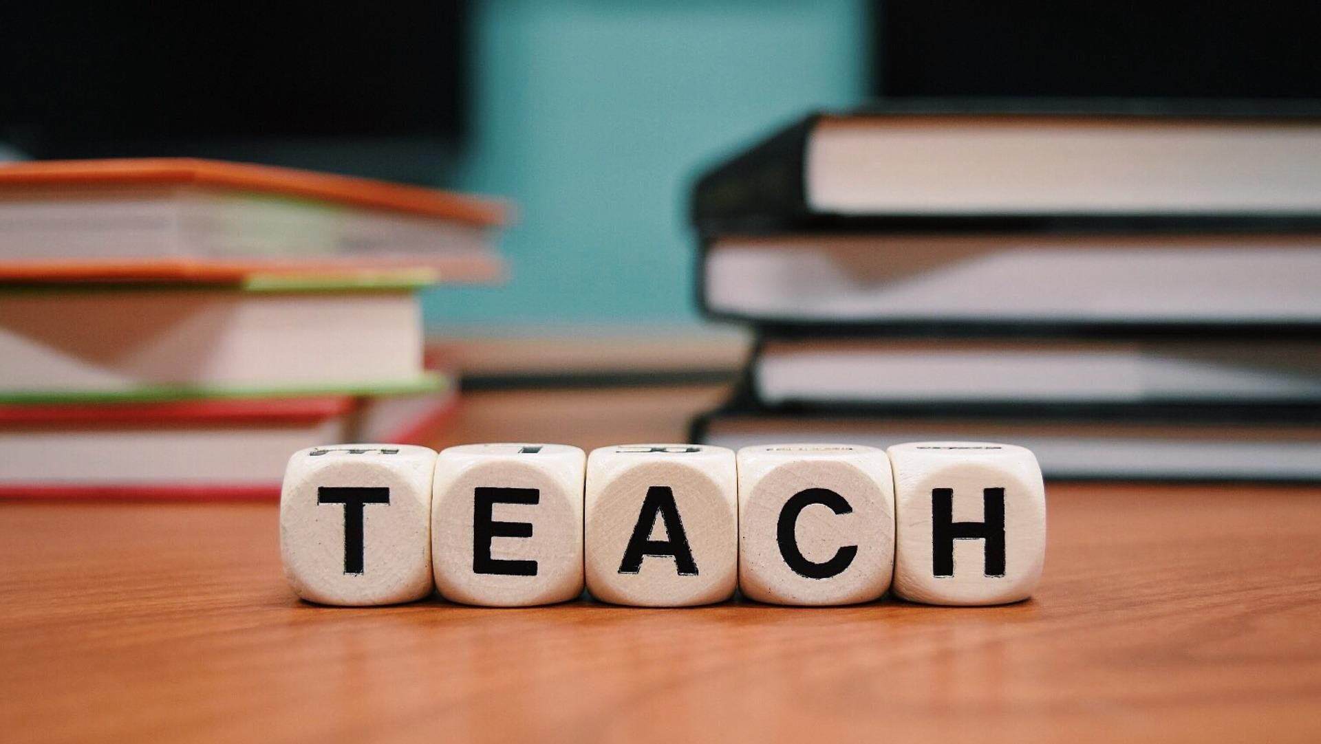 The word teach spelled out in blocks in front of stack of books