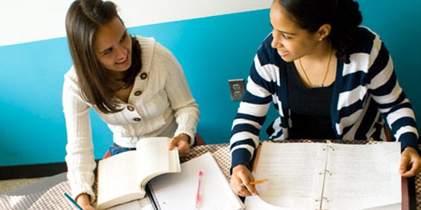 Two students taking notes and looking at each other.