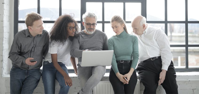 Five people sitting on a windowsill looking at a laptop.