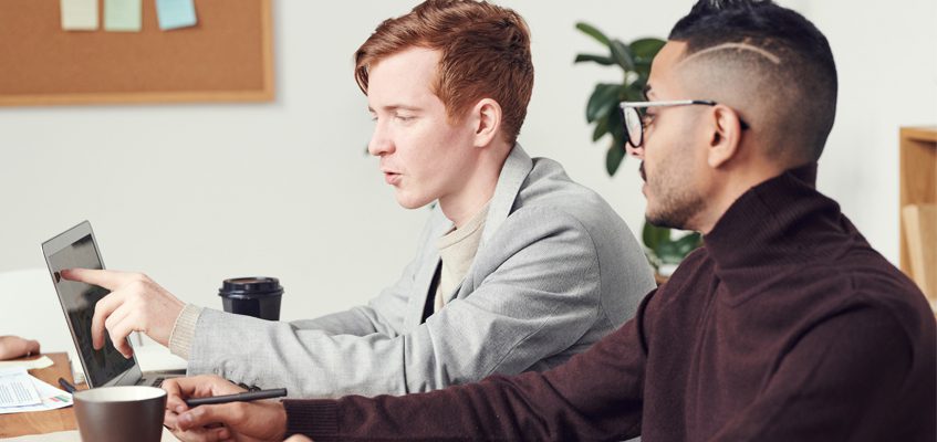 Two people having a conversation and looking at a laptop.