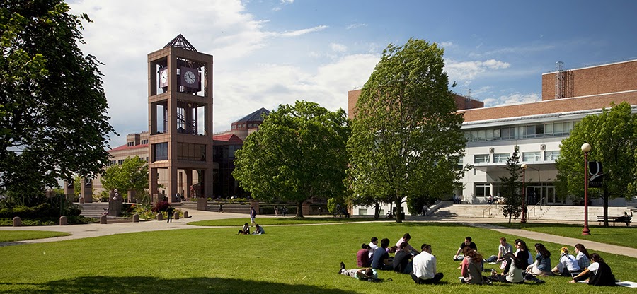 A scenic shot of Queens College Campus. A scenic shot of Queens College Campus with the Benjamin S. Rosenthal Library in the background and people sitting on the grass in the foreground.