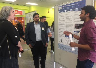 A person presenting a poster labeled “Peer Mentors as General Student Advisors” to the two people observing him.