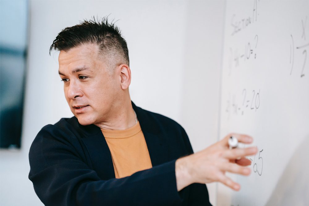 Person holding a marker pointing to a whiteboard. 