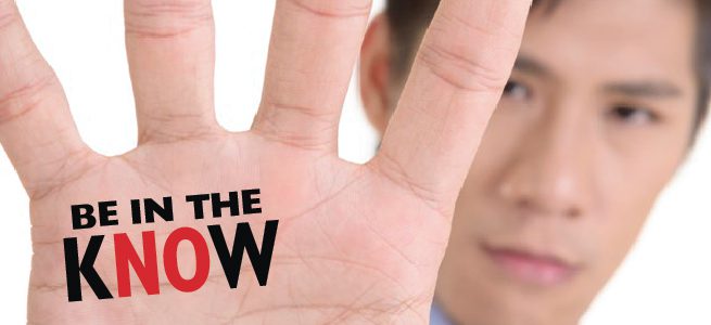 A man holds up his hand, palm facing the camera with fingers outstretched. “Be in the Know” is written in the palm on his hand.