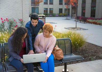 A group of people looking at a laptop while sitting outside.