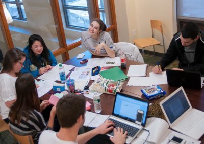 Group of people studying at a table with laptops and open books.