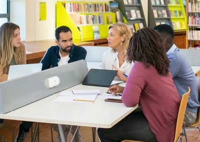 Five students sitting at a table in a library.