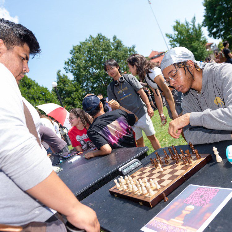 Club Day Chess - 2024 Two students looking at a laptop while sitting on the grass.