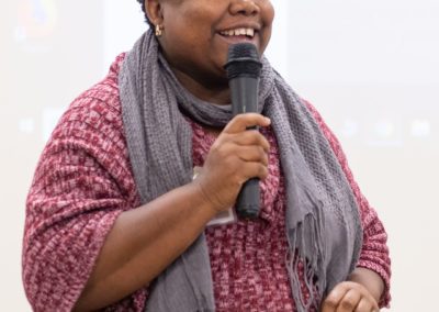 A person standing and talking while holding a microphone.
