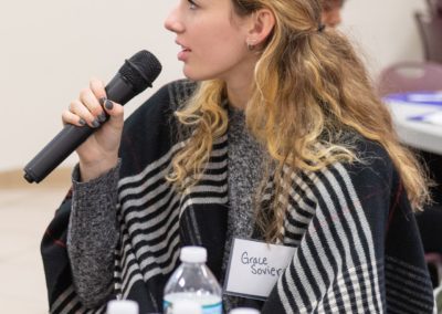 A person sitting at a table and talking while holding a microphone.