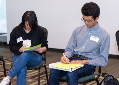 Two people sitting in chairs next to each other taking notes.