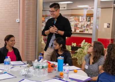 A person standing and talking to a table of people.