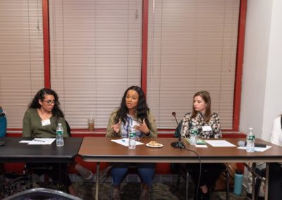 Five people sitting at a table with microphones. The person in the center is speaking.